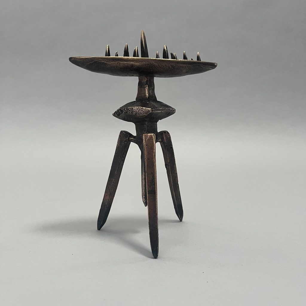 A freestanding small bronze sculpture depicting a boat filled with aspirational steeple like vertical spikes, supported on a geometric form symbolising the world.. both supported on a tripod of spikes